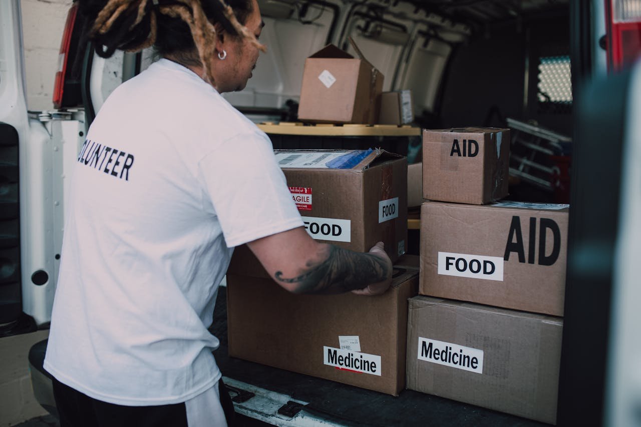 Services-03 A volunteer organizes aid boxes containing food and medicine in a van for community service.