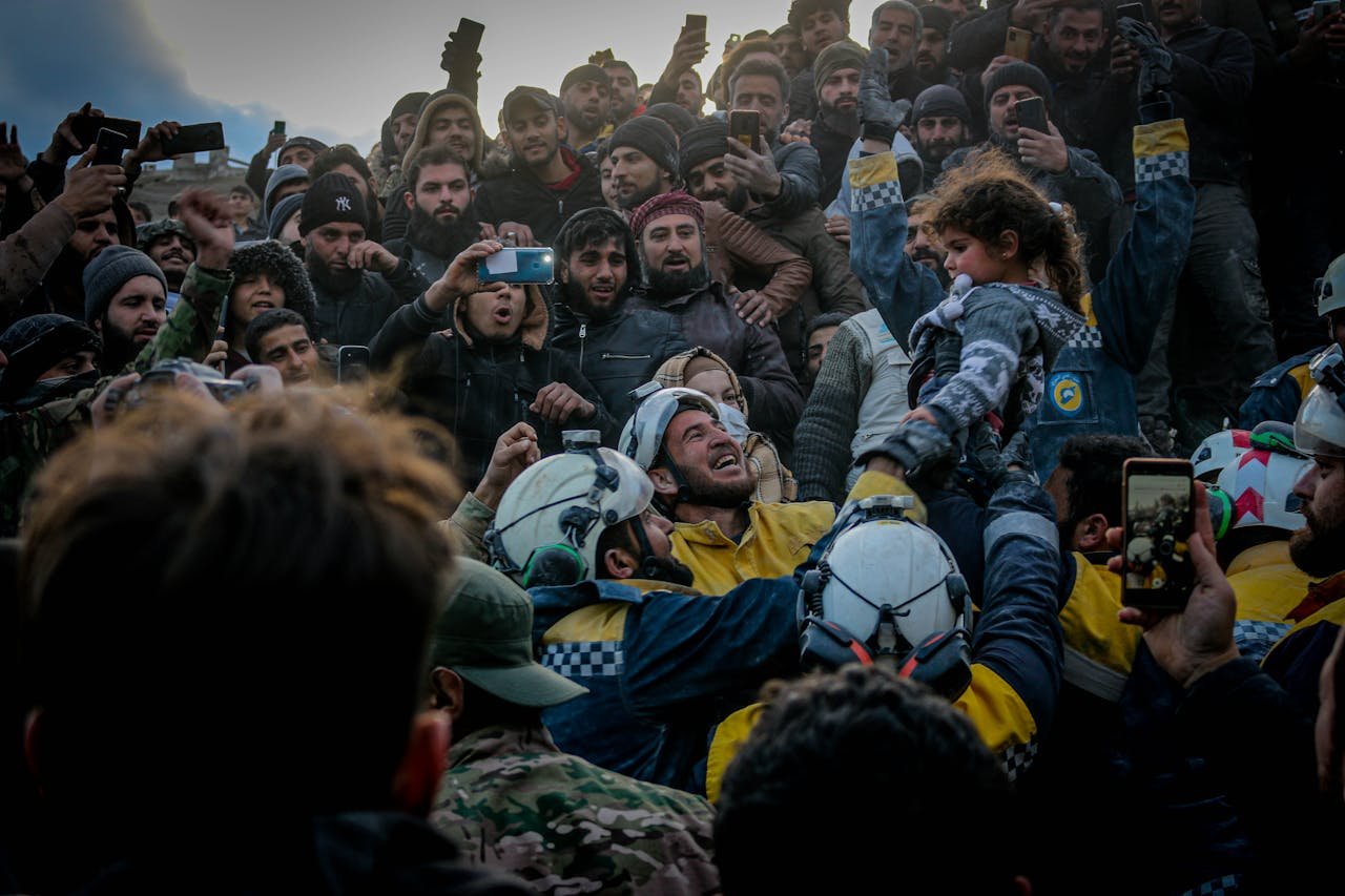 creative Rescue workers celebrate saving a child in Idlib, Syria amid a supportive crowd.